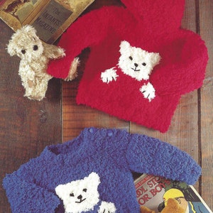 May include: Two knitted baby sweaters with a white bear applique on the front. One sweater is red with a hood and the other is blue. Both sweaters are made with a fluffy yarn.