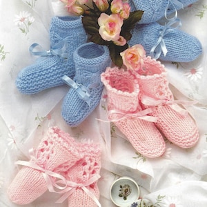 May include: A pair of blue knitted baby booties with white stitching and a pair of pink knitted baby booties with white lace trim. Both pairs have satin ribbon ties.
