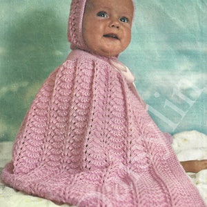 以下が含まれることがあります： 繊細なレース模様のピンクのニット製ベビーボンネットとケープ。ボンネットは先のとがったトップで、あごの下で結ばれます。