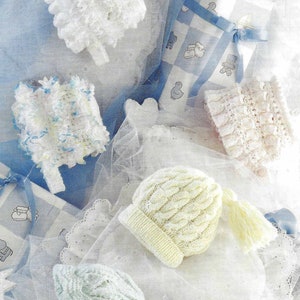 May include: Five crocheted baby hats in various colors and styles, including white, light blue, pink, and cream. The hats are arranged on a white background with blue and white wrapping paper and a silver star.