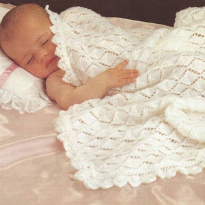 May include: A white crocheted baby blanket with a delicate lace trim. The blanket is draped over a sleeping baby.