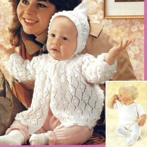 May include: A white knitted baby cardigan with a bobble stitch pattern and a matching bonnet. The cardigan has a button closure and is shown on a baby wearing a pink onesie.