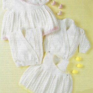 May include: Three white knitted baby garments: a dress, a cardigan, and a sleeveless dress. The garments are made with a delicate lace pattern and have a soft, feminine look.