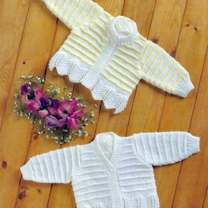 May include: Two knitted baby cardigans, one white and one with yellow stripes. Both cardigans have a scalloped hem and button closure.