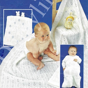 Puede incluir: Un bebé está sentado sobre una manta blanca de punto calado. La manta tiene un patrón repetido de pequeñas formas de hojas. También se ven un pequeño conejito de peluche y una muñeca. Un bebé lleva un saco de dormir de punto blanco.