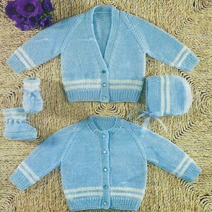 May include: Two knitted baby cardigans with white stripes, one with a button-up front and one with a crew neck. The cardigans are laid out on a woven straw surface. There are also two knitted booties and a knitted hat with white stripes.
