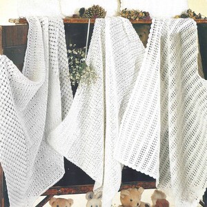 May include: Four white crocheted blankets draped over a wooden cabinet with the word "CROCHET" in the top right corner. The blankets are displayed with stuffed animals and flowers in the foreground.