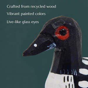 K&ouml;nnte beinhalten: Eine handgeschnitzte Vogelfigur aus Holz mit schwarzem Kopf, rotem Auge und wei&szlig;er Brust mit schwarzen Markierungen. Der Text lautet: Hand-carved artisan charm, Crafted from recycled wood, Vibrant painted colors, Live-like glass eyes.