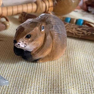 A hand-carved wooden figurine of a brown and gray squirrel. The squirrel is sitting on a light brown surface.