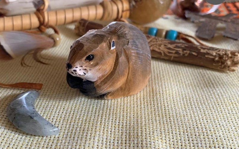 A hand-carved wooden figurine of a brown and gray squirrel. The squirrel is sitting on a light brown surface.