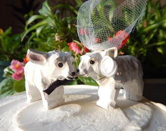 Può includere: Topper per torta nuziale in ceramica bianca con un agnello con papillon nero e una sposa agnello in ceramica bianca con velo bianco. La sposa agnello indossa una fascia bianca con un fiore bianco.