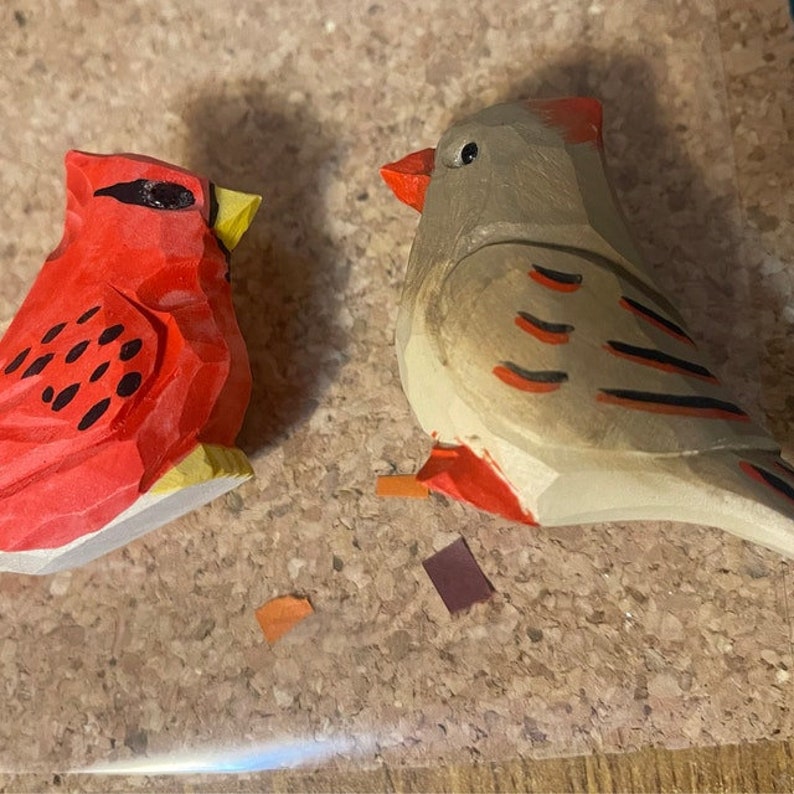 Two wooden bird figurines, one red with black spots and one gray with red and black stripes.