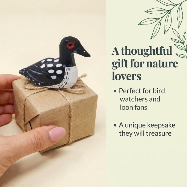 May include: A hand-carved wooden loon figurine with black, white, and red painted details, perched atop a small square box wrapped in brown paper and tied with rustic twine. The text reads: A thoughtful gift for nature lovers.