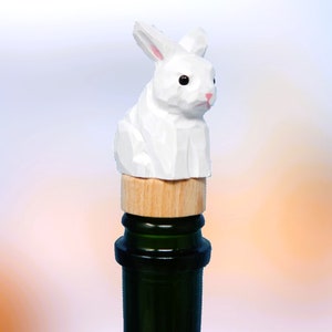 May include: White wooden rabbit bottle stopper with a wooden base. The stopper is on top of a green wine bottle.