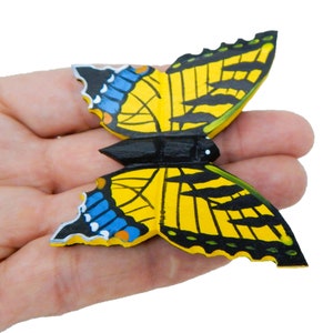 May include: A wooden butterfly ornament painted in yellow, black, and blue. The butterfly has a detailed wing pattern and a black body.