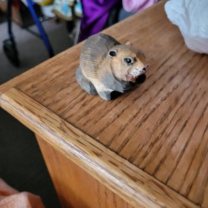 A small, wooden carving of a brown and gray squirrel sitting on a wooden surface.