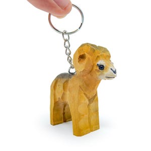 May include: A wooden keychain shaped like a brown ram with a silver key ring. The ram has a detailed face and horns.