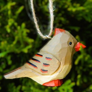 A wooden cardinal Christmas ornament with red, black, and white painted details. The ornament is hanging from a twine string.
