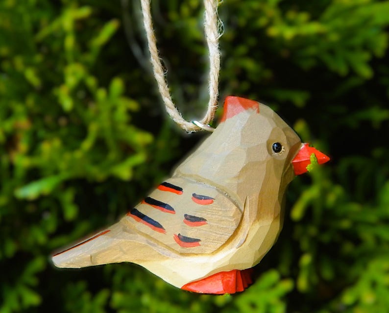 A wooden cardinal Christmas ornament with red, black, and white painted details. The ornament is hanging from a twine string.