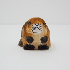 A hand-carved wooden beaver figurine with brown and black paint details. The beaver has a white face with black eyes and a black nose.