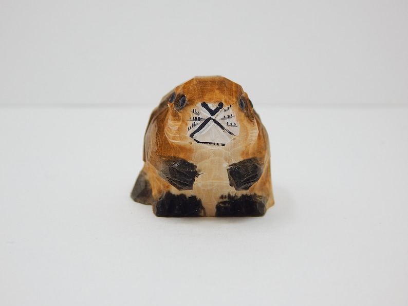 A hand-carved wooden beaver figurine with brown and black paint details. The beaver has a white face with black eyes and a black nose.