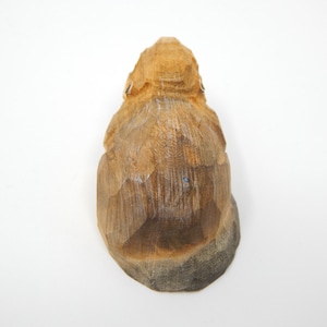 A wooden carving of a small animal, possibly a squirrel or a rabbit, with a light brown color and a rough, textured surface.