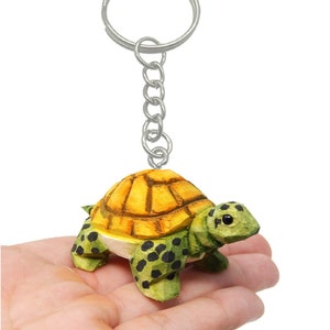 May include: A small, hand-carved wooden turtle keychain with a yellow shell, green body, and black spots. The turtle is attached to a silver key ring.