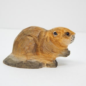 A hand-carved wooden beaver figurine. The beaver is brown with black eyes and a black nose. It is sitting on its haunches with its tail behind it.