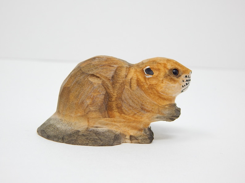 A hand-carved wooden beaver figurine. The beaver is brown with black eyes and a black nose. It is sitting on its haunches with its tail behind it.