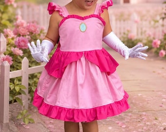 May include: A pink dress with ruffled shoulder straps, a central oval blue brooch, and a layered skirt with a dark pink hem. The outfit includes white elbow-length gloves, a matching pink hair bow, and sandals with decorative butterfly accents.