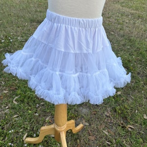 May include: White tulle petticoat with a ruffled hem. The petticoat is on a wooden display stand.