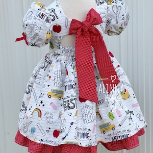 May include: A white dress with a red bow and a school-themed print. The print includes phrases like "Hey Phi Hello", "I can do anything", and "You're the best".