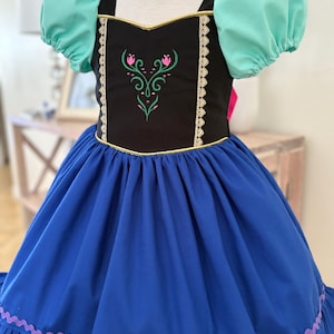 May include: A blue and black dress with a floral design. The dress features a black bodice with gold trim and a floral embroidery. The sleeves are mint green, and the skirt is blue with a ruffled hem. A children's dress.