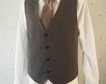May include: A dark gray vest featuring a V-neckline and four black buttons down the front. The vest is worn over a crisp white long-sleeved collared shirt, which is paired with a solid light brown necktie featuring a subtle white dotted pattern.