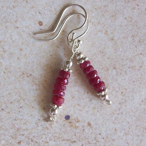 May include: A pair of silver dangle earrings with red gemstone beads. The earrings have a simple hook closure.