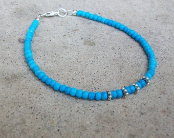 May include: A turquoise blue beaded bracelet with silver accents. The bracelet is made of small, round beads and has a silver clasp.