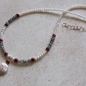 May include: A delicate necklace with a pearl pendant, featuring white pearls, gray and red beads, and a silver chain.