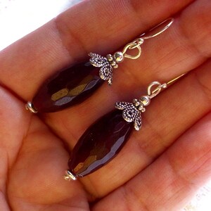 May include: A pair of dangle earrings with dark purple faceted gemstone beads and silver filigree accents.