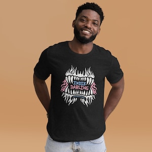 May include: Dark gray t-shirt with a graphic design featuring a stylized mouth with teeth, flames, and the text "Indie Darling San Francisco" in blue and pink. The shirt is a crew neck style.