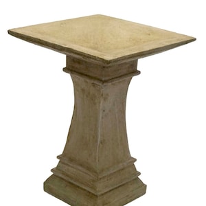 May include: A light brown concrete bird bath with a square base and a square top. The bird bath has a simple design with a slightly flared base and a flat top.