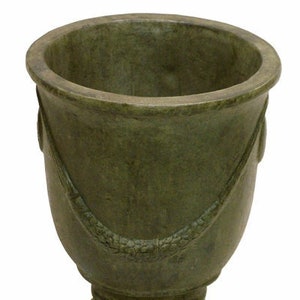 May include: A green, round, ceramic planter with a decorative design around the top edge. The planter has a wide base and a narrow opening.