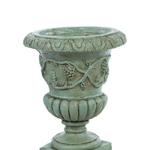 May include: A green ceramic planter with a detailed vine design. The planter has a wide, round top and a base with a square shape.