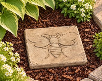 May include: A square, light brown stone garden stepping stone featuring a relief carving of a bee in the center. The bee design shows detailed wings and a segmented body, with a textured surface that mimics natural stone material.