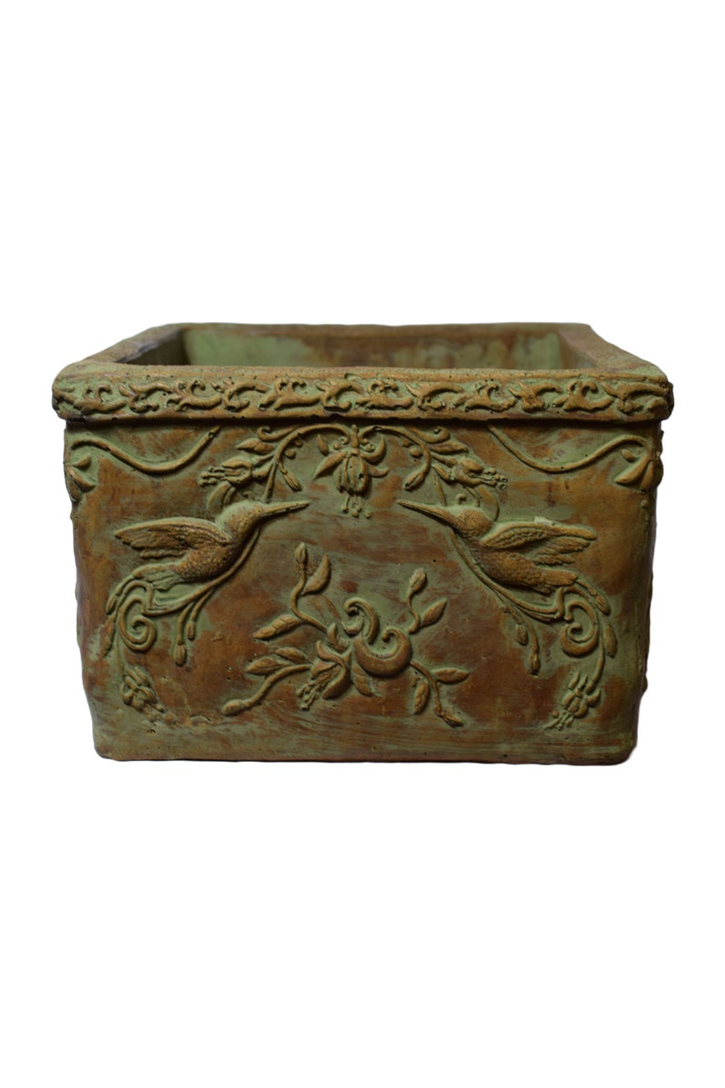 May include: Rectangular planter with a distressed brown and green finish. The planter features embossed hummingbird and floral designs. The top edge has a decorative border. Suitable for indoor or outdoor use.