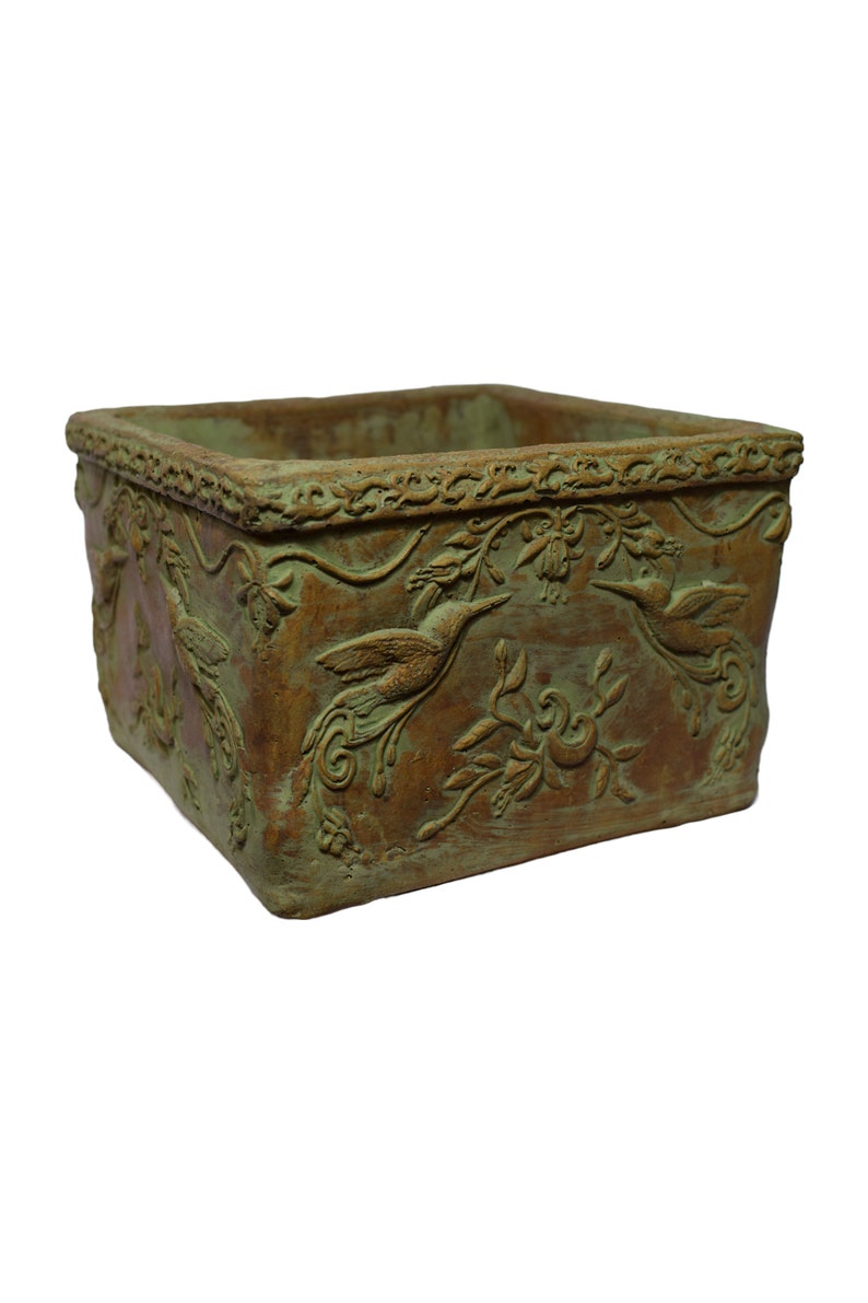 May include: Square planter with a distressed finish, featuring a hummingbird and floral relief pattern. The planter has a brown base with green highlights, and a decorative border. Suitable for gardens or interior spaces.
