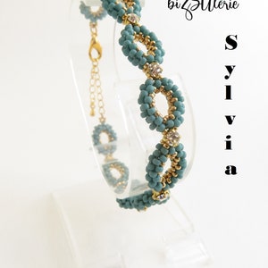 May include: A teal and gold beaded bracelet with a clasp closure. The bracelet features a repeating pattern of small beads and larger beads with clear rhinestones.