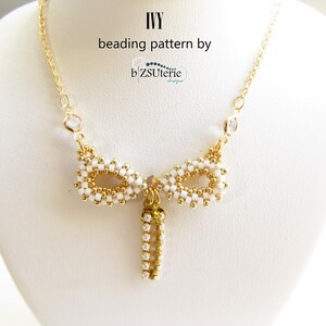 Könnte beinhalten: Eine goldfarbene Halskette mit ovalen Akzenten aus weißen und goldenen Perlen und einem hängenden Anhänger. Die Halskette trägt den Text "IVY beading pattern by b'ZSUterie design". Die Halskette wird auf einer weißen Schaufensterpuppe präsentiert.