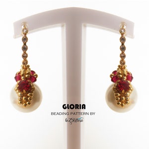 May include: A pair of gold and red beaded earrings with a pearl drop. The earrings are on a white display stand. The text "GLORIA BEADING PATTERN BY bizSlitterie" is below the earrings.