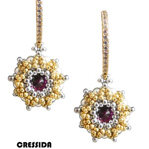 May include: A pair of gold earrings with a purple gemstone center and a white pearl border. The earrings are made with small beads and have a dangling design.