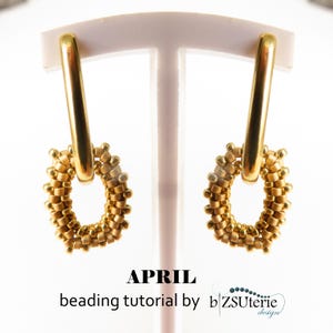 Puede incluir: Un par de pendientes dorados. Cada pendiente presenta una parte superior rectangular y una parte inferior en forma de aro con cuentas. La palabra "APRIL" y el texto "beading tutorial by b ZSUtérie design" están impresos en la parte inferior.